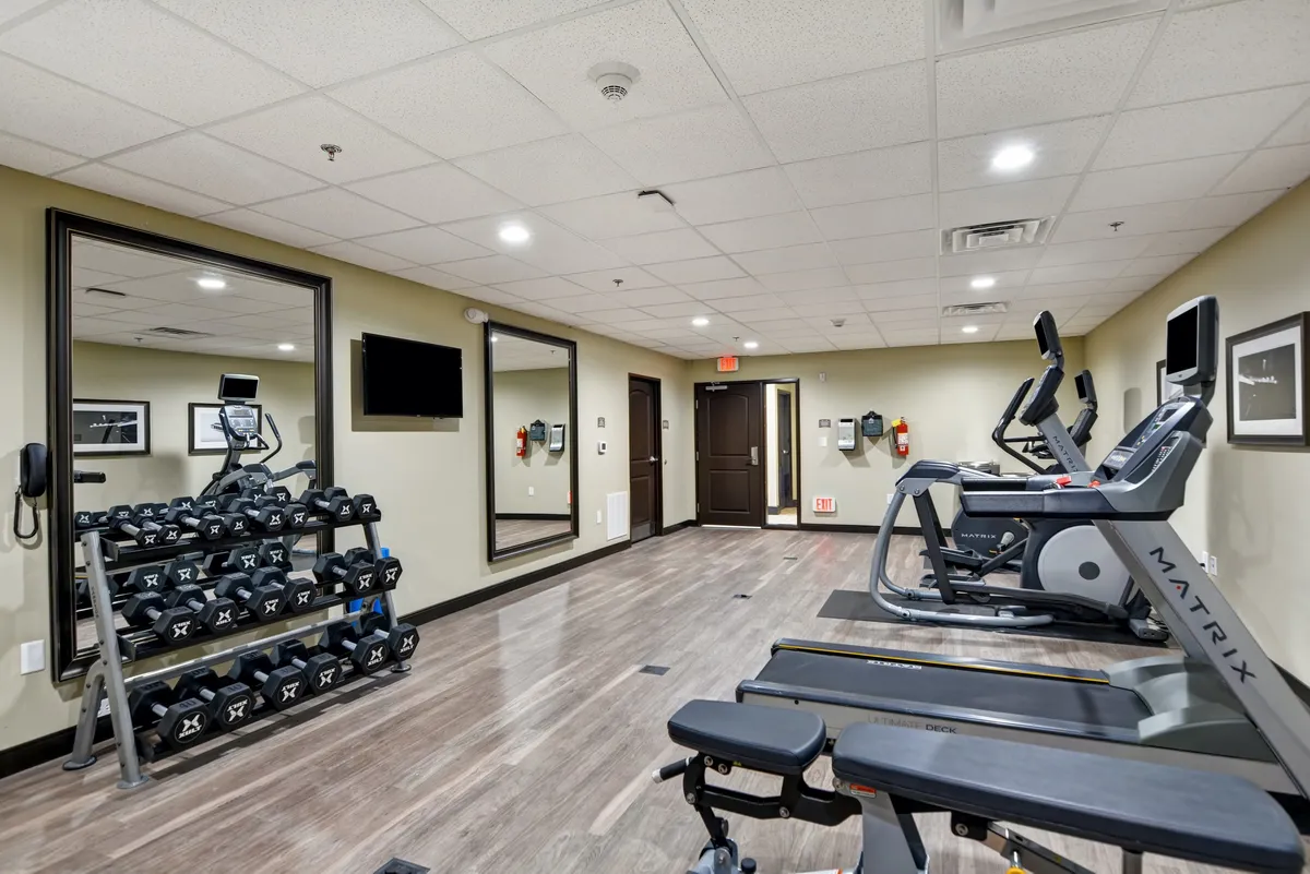 This image shows a modern fitness center complete with a dumbbell rack, exercise machines, and mirrors. The space is bright and organized, inviting guests to energize before exploring the local scene or unwind after a day of activities.