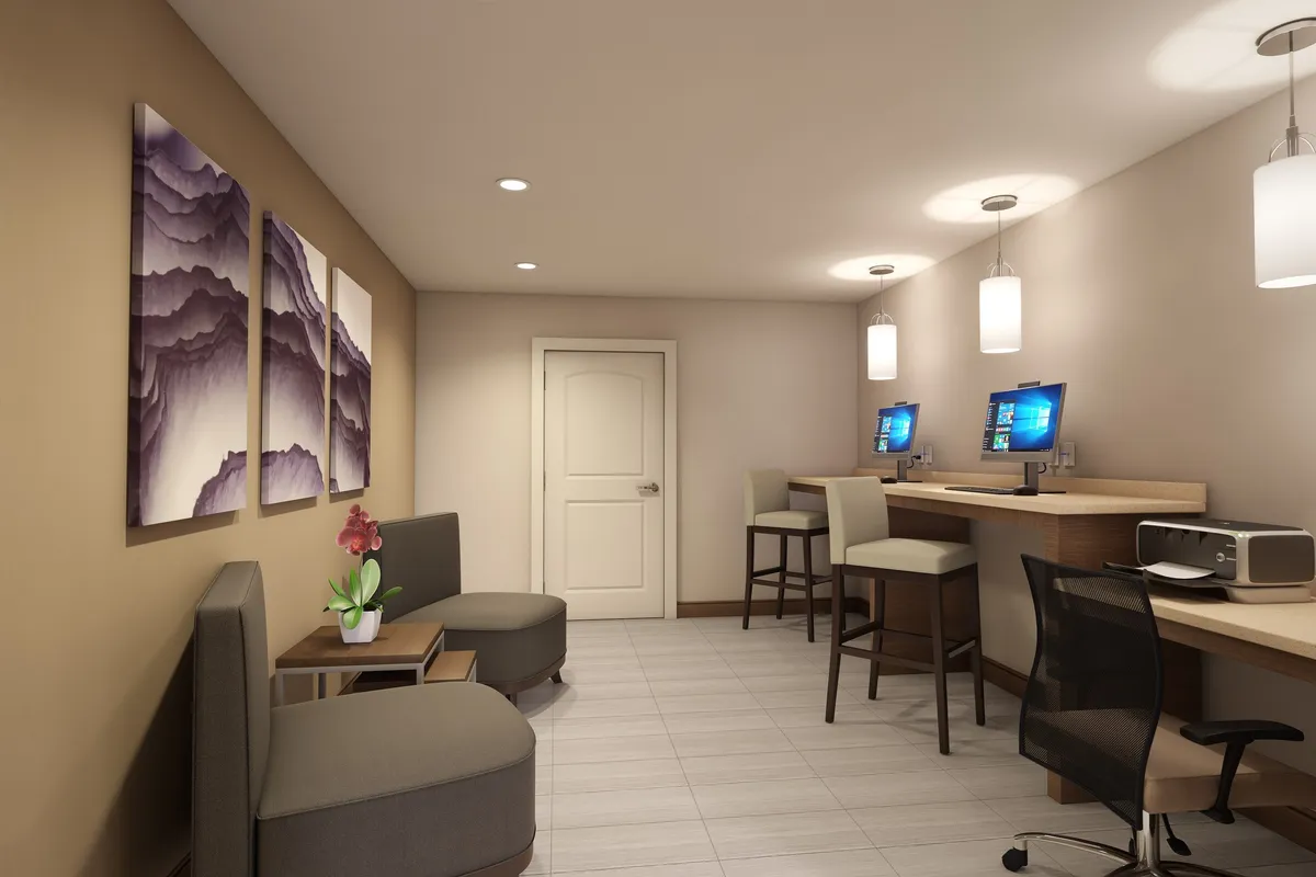 A professional yet inviting workspace featuring computers, a comfortable seating area, and decorative artwork on the wall. The space is well-lit and conducive to productivity, ideal for business travelers or digital nomads.
