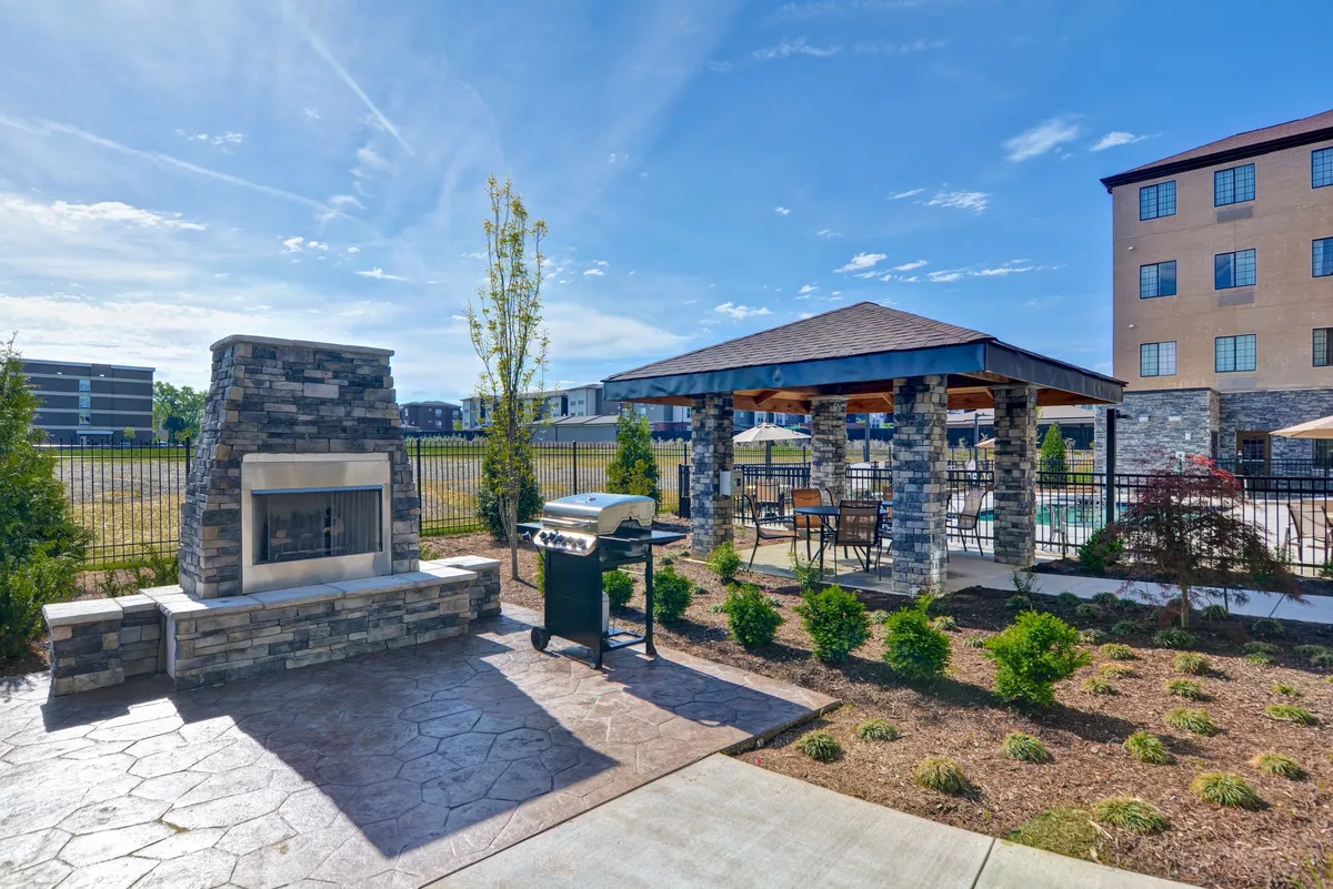 An inviting outdoor area featuring a stone fireplace, grill, and gazebo. The space is clearly designed for gatherings, barbecues, and relaxed family moments. Surrounded by greenery, the approachable setting connects the property to the outdoors and suggests opportunities for summer fun.