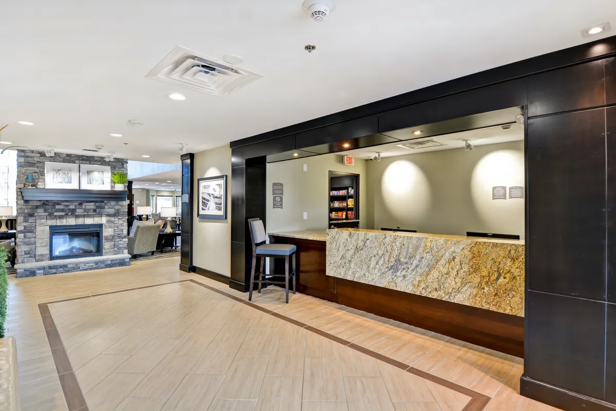The image depicts a warmly lit reception area with a welcoming desk, a cozy fireplace, and comfortable seating. The space invites guests to relax, socialize, or await check-in, setting a positive first impression. The fireplace adds a touch of comfort and romance, aligning with the getaway theme.